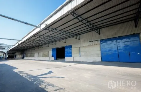 Warehouse for rent in Pathum Thani - Long warehouse facade featuring multiple loading bays and a wide truck driveway.