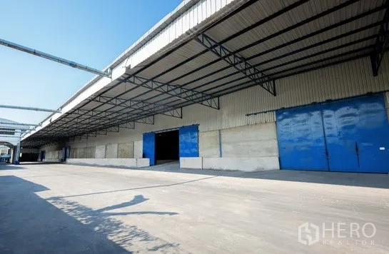 Warehouse for rent in Pathum Thani - Long warehouse facade featuring multiple loading bays and a wide truck driveway.