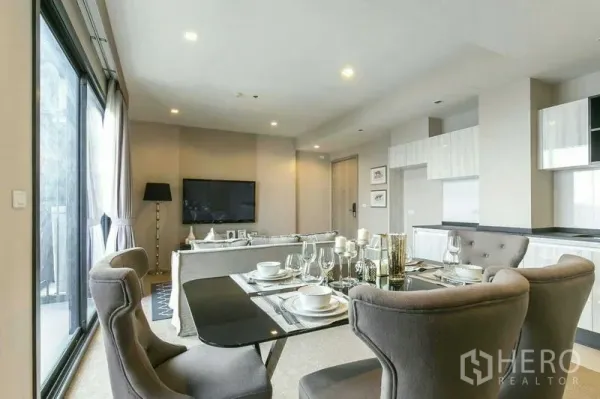 Condominium for rent or sale in Watthana, Bangkok - Open-plan living and dining room with set table, sofa, TV, and large sliding doors to the balcony.