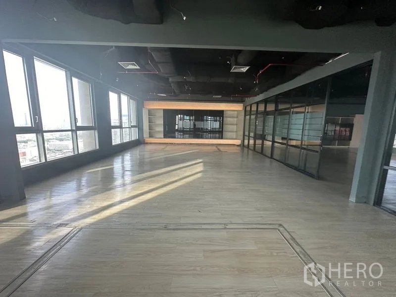 Office Space for rent in Bang Rak, Bangkok - Large open-plan workspace with wood flooring, floor-to-ceiling windows and black exposed ceiling.