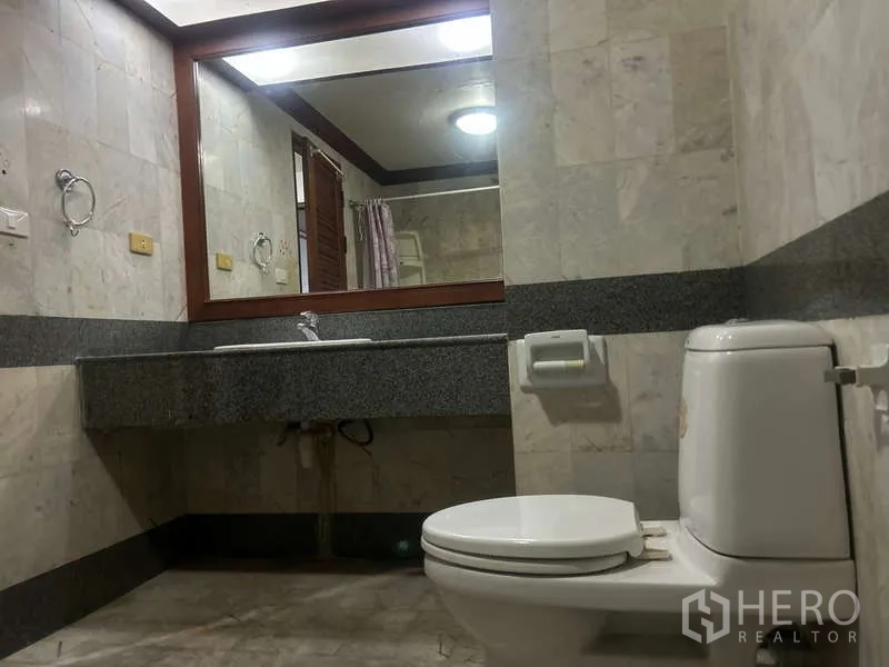 Condominium for sale in Huai Khwang, Bangkok - Marble-tiled bathroom with oversized mirror, vanity counter, and toilet.