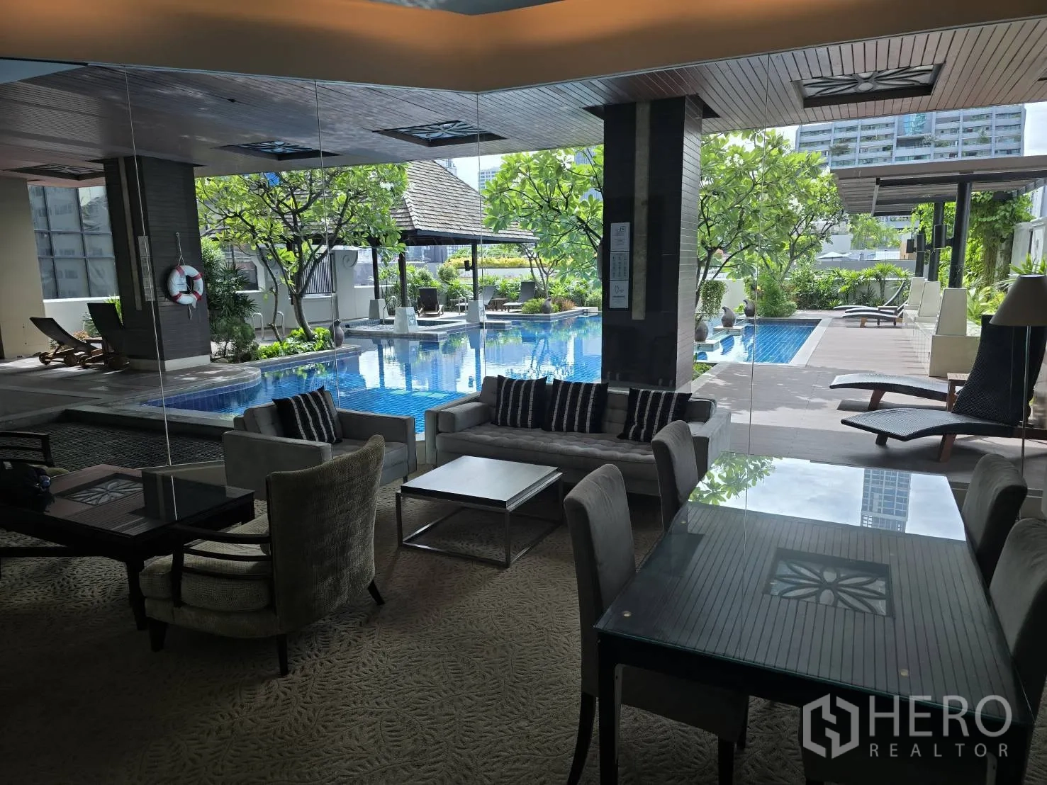 คอนโด for rent or sale in Watthana, Bangkok - เลานจ์มองเห็นสระว่ายน้ำกลางแจ้งพร้อมเตียงอาบแดดและต้นไม้ร่มรื่น.