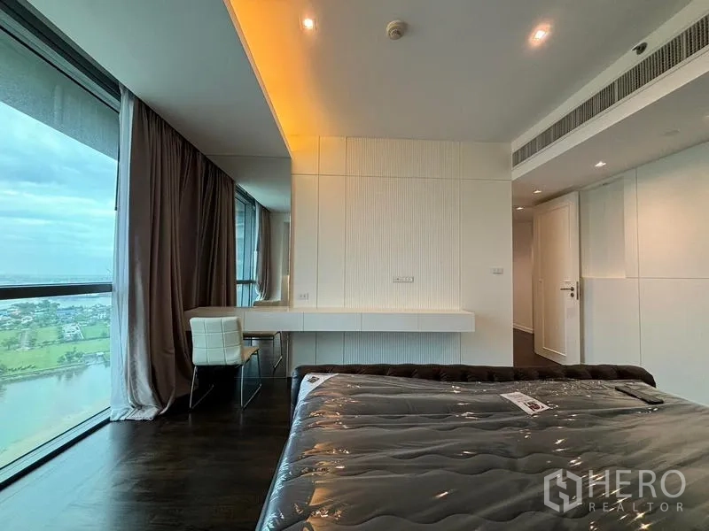 Condominium for rent - Corner bedroom with a desk by panoramic windows facing the Chao Phraya River.