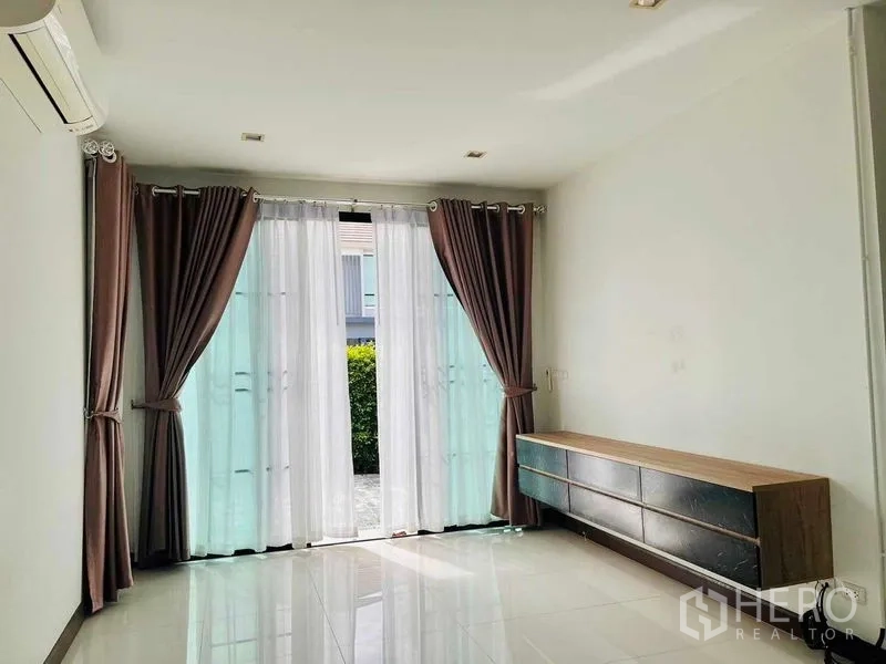 Detached House for rent or sale in Thanyaburi, Pathum Thani - Downstairs room with glass doors opening to a patio and a built-in low cabinet.