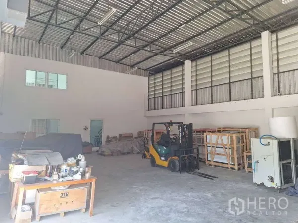 Warehouse for sale in Pathum Thani - Spacious warehouse interior with high steel roof, ventilation panels and a forklift beside storage racks.