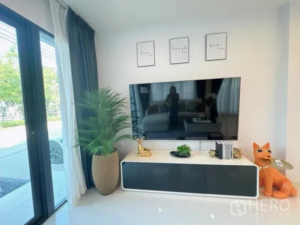 Detached House for rent or sale - Sunlit living corner with large flat-screen TV on sleek console, tall windows and indoor plant.