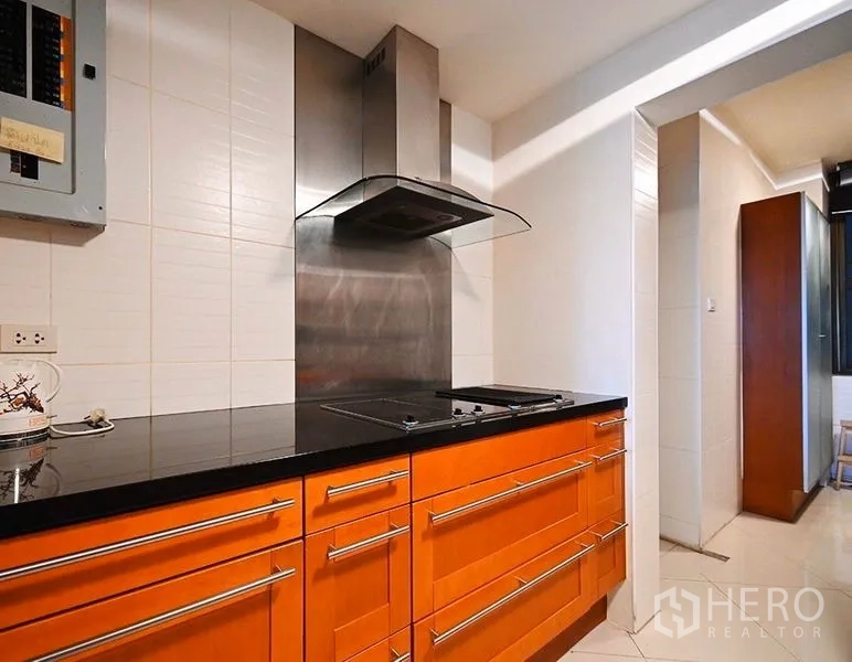 Condominium for rent in Pathum Wan, Bangkok - Modern kitchen with black granite countertop, stainless range hood over an induction cooktop, and orange cabinetry.