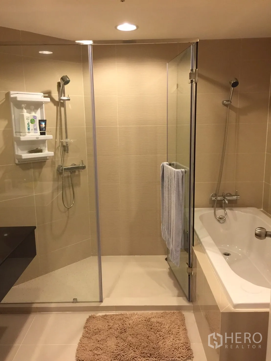 Condominium for rent in Huai Khwang, Bangkok - Bathroom with separate glass shower and built-in bathtub in beige tiles.