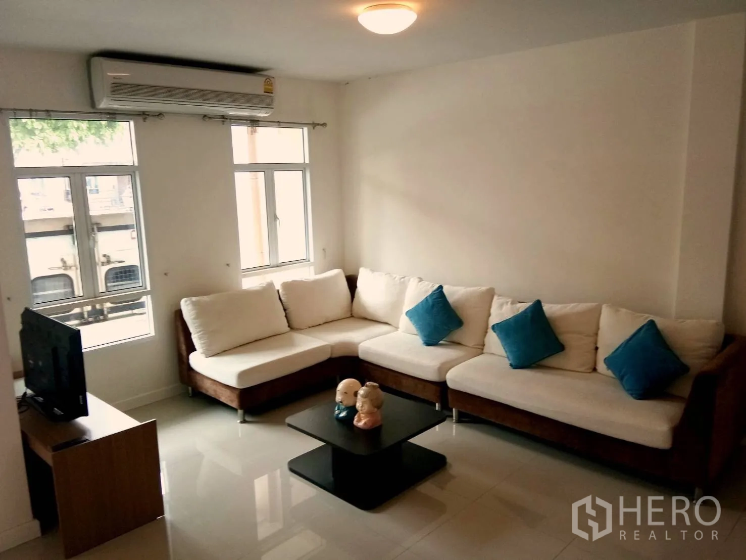 联排别墅 出租在Watthana, Bangkok - 带空调的客厅，L形沙发、电视柜与大窗户。