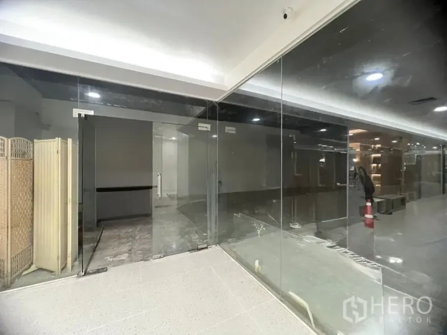 零售空间 出租在Khlong Toei, Bangkok - 无框玻璃门面与双开门，通向明亮走廊内的空置商铺。