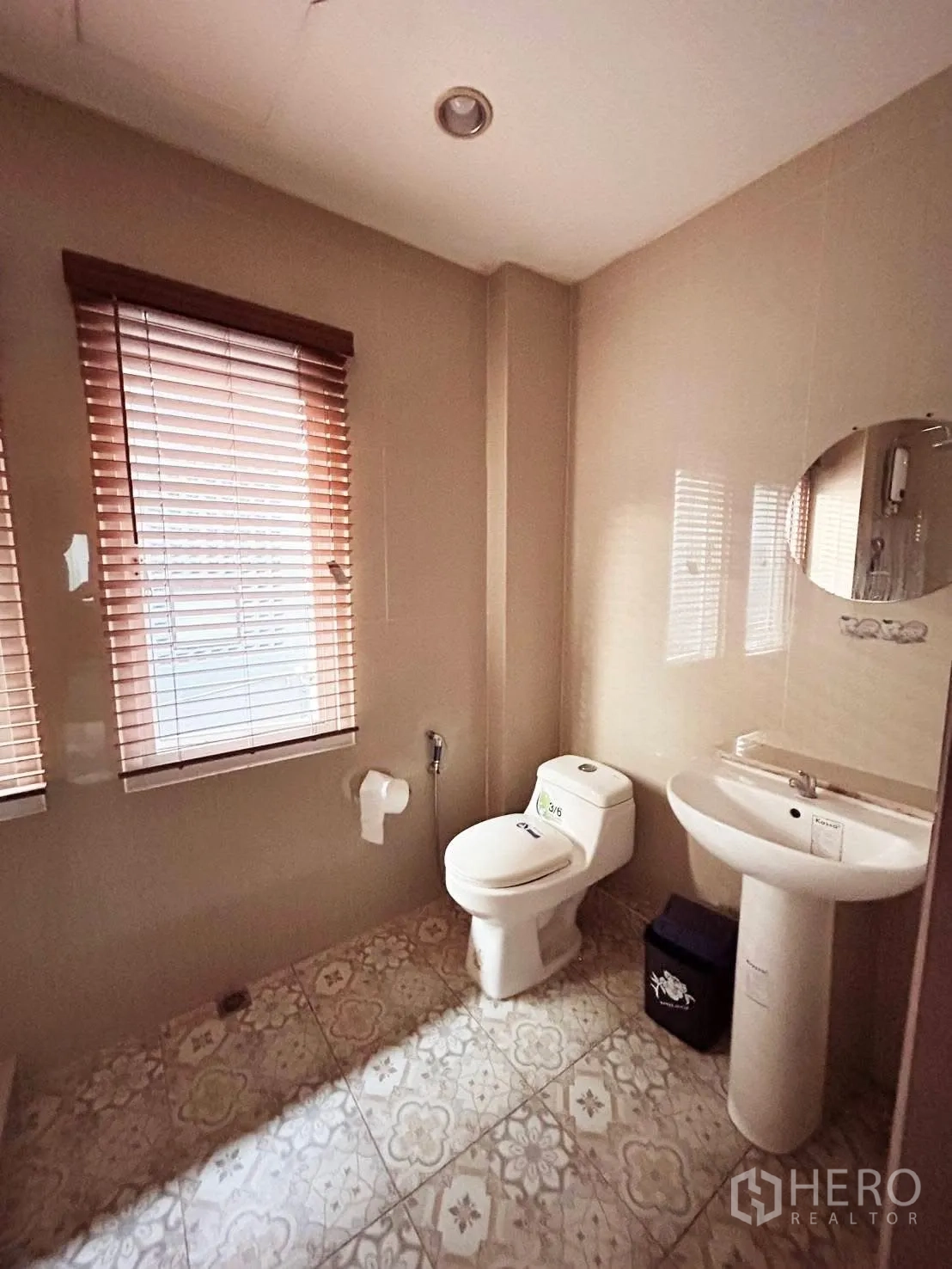Detached House for rent or sale in Wang Thonglang, Bangkok - Neutral-tone bathroom with patterned floor tiles, pedestal sink, toilet and two windows with blinds.