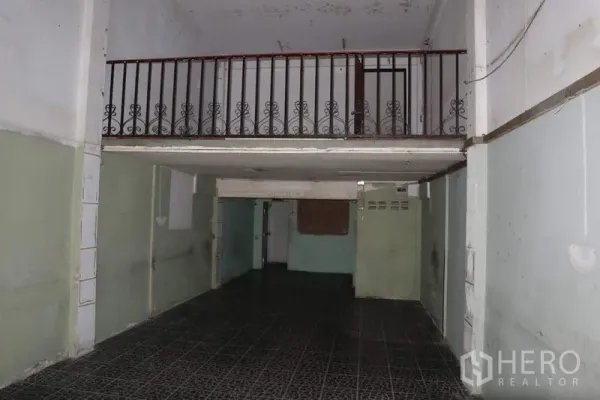 Shophouse for sale in Huai Khwang, Bangkok - Ground-floor hall with dark tiled flooring and a mezzanine with metal railing, suitable for retail or workspace.