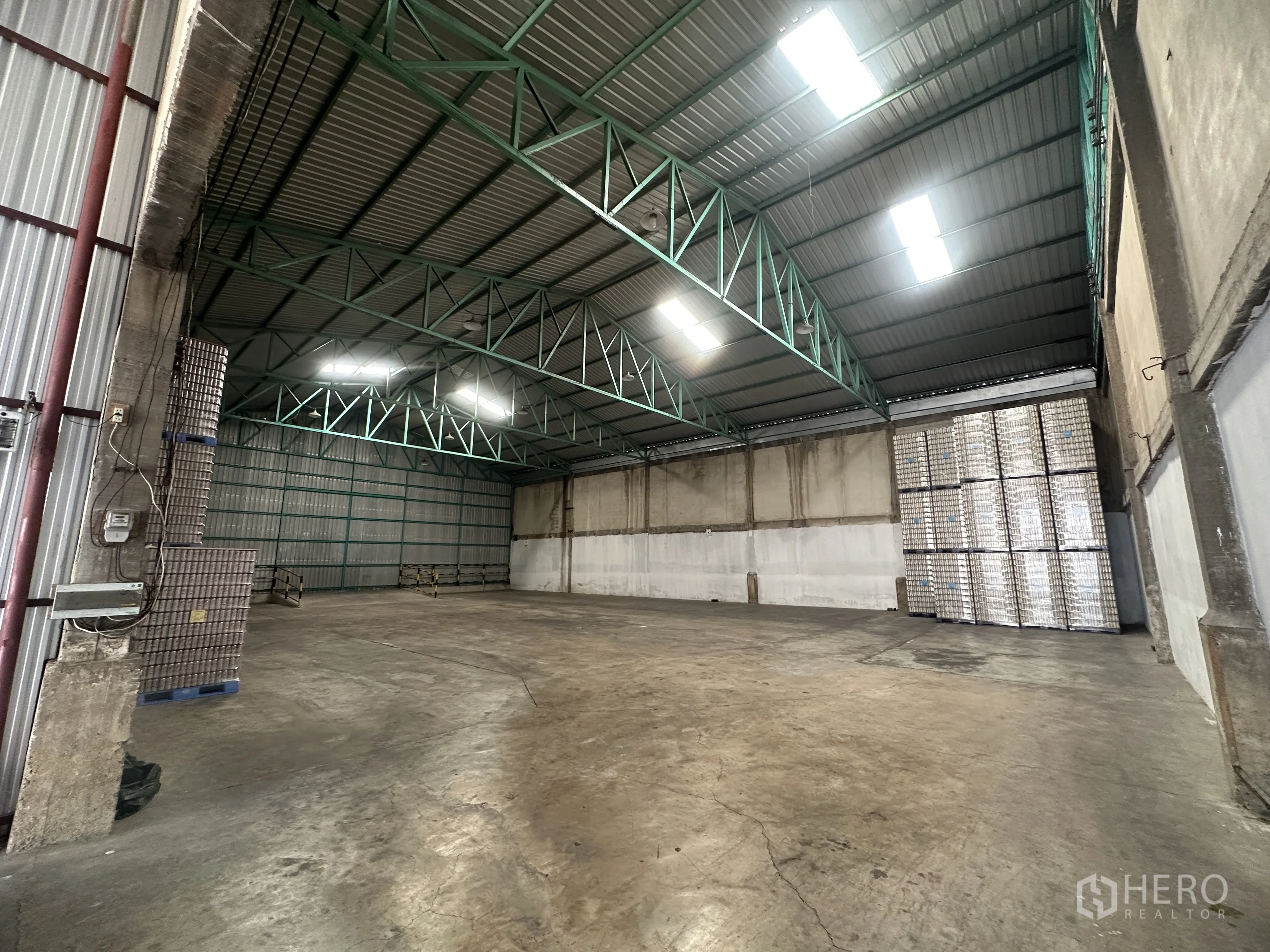 货栈 for rent in Mueang Pathum Thani, Pathum Thani - 室内无柱大跨度视角，明亮屋面采光板，后墙堆放托盘。