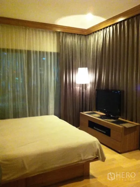 Condominium for rent or sale in Watthana, Bangkok - Cozy master bedroom with large window, layered curtains, warm lighting and a TV console.