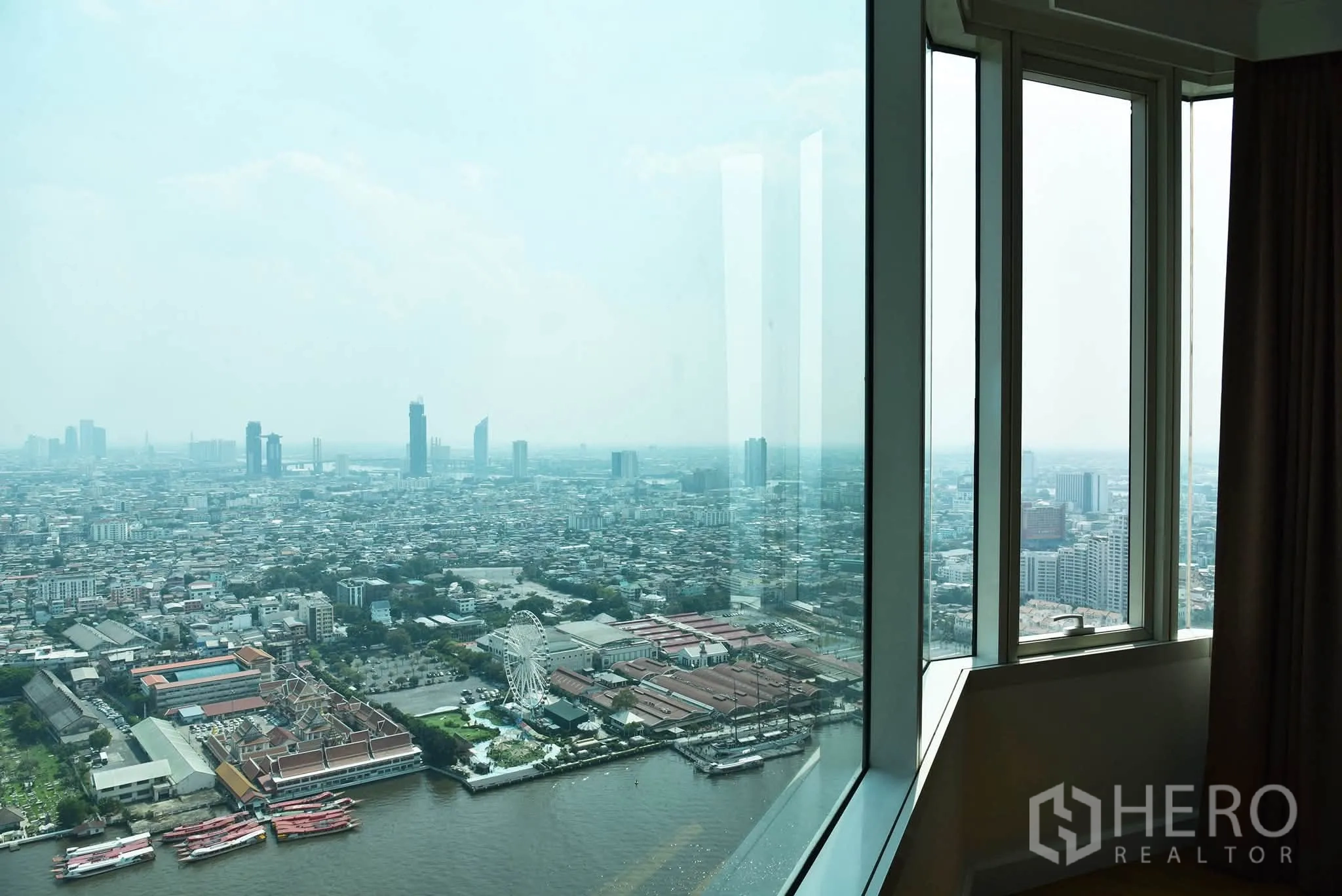 Condominium for sale in Khlong San, Bangkok - Corner floor-to-ceiling window showing a wide cityscape and river with a ferris wheel in view.