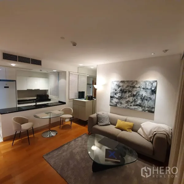 Condominium for rent in Watthana, Bangkok - Cozy lounge with sofa, mirror wall, artwork and warm lighting next to the kitchen.