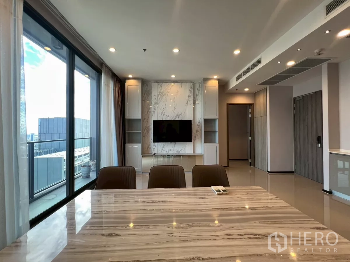 Condominium for rent in Phra Khanong, Bangkok - Dining table view toward TV wall and balcony with full-height glazing.