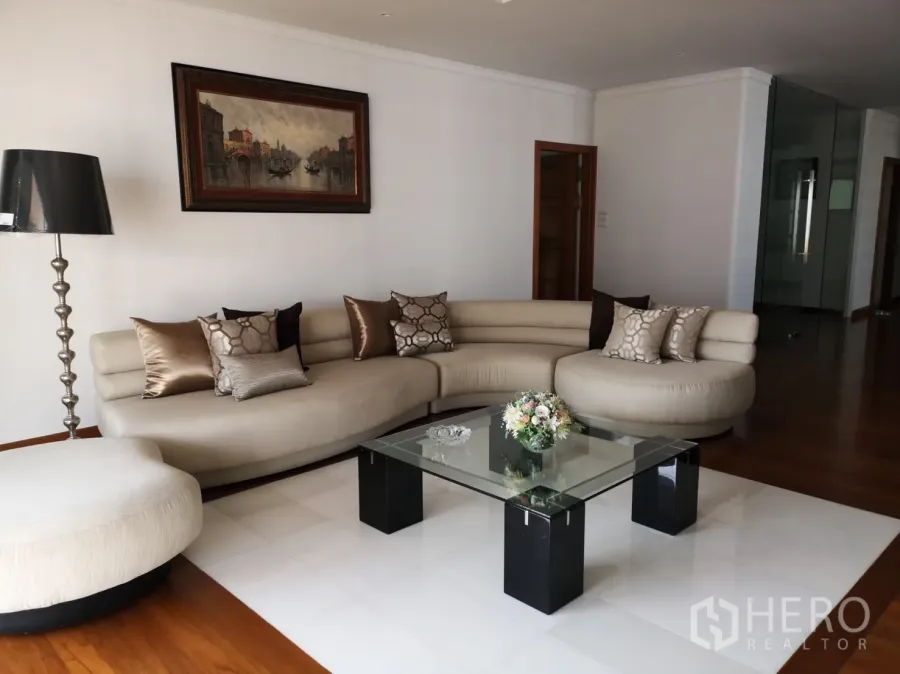 คอนโด ให้เช่าในBangkok - ห้องนั่งเล่นกว้าง โซฟาทรงโค้งสีครีม โต๊ะกลางกระจก พื้นไม้