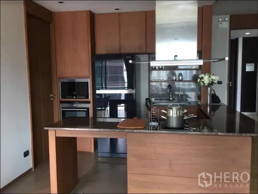 Condominium for rent in Watthana, Bangkok - Modern open kitchen with wood cabinetry, stone island, built-in oven and range hood.