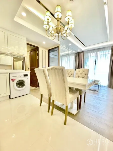 Condominium for sale in Huai Khwang, Bangkok - Dining area with chandelier next to compact kitchen and washing machine.