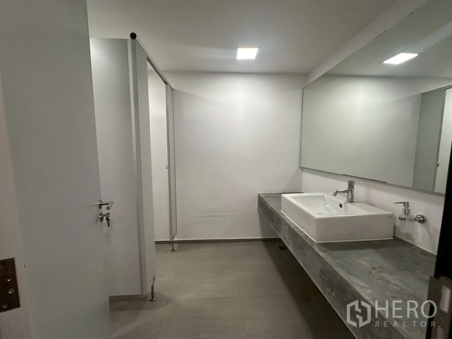 Office Space for rent - Restroom corridor with white partitions and a basin on stone counter.