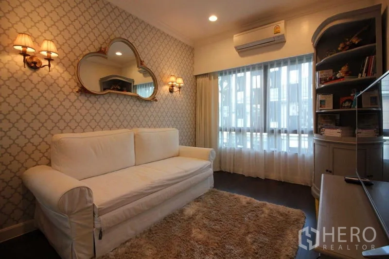 独立式住宅 出租在Prawet, Bangkok - 舒适客厅，白色沙发、几何墙纸与壁灯。