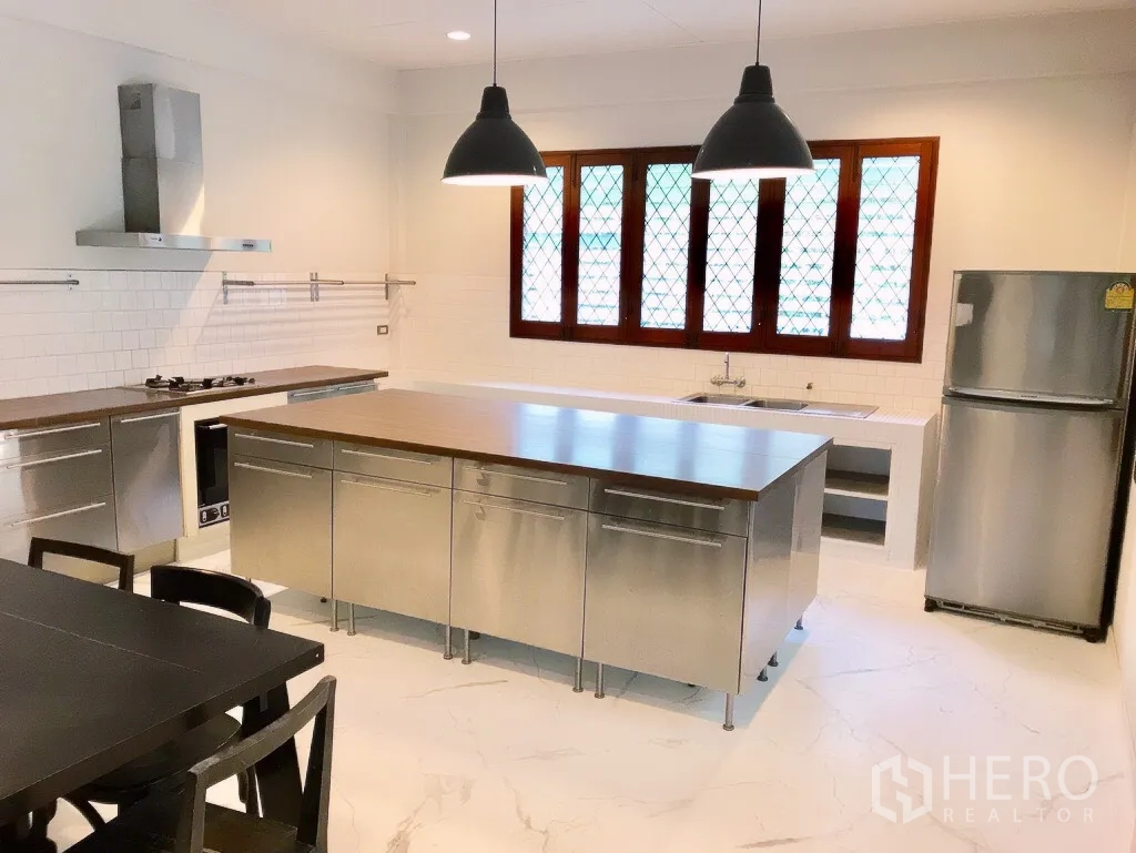Detached House for rent in Khlong Toei, Bangkok - Modern kitchen with stainless-steel island, pendant lights, and wide lattice windows.