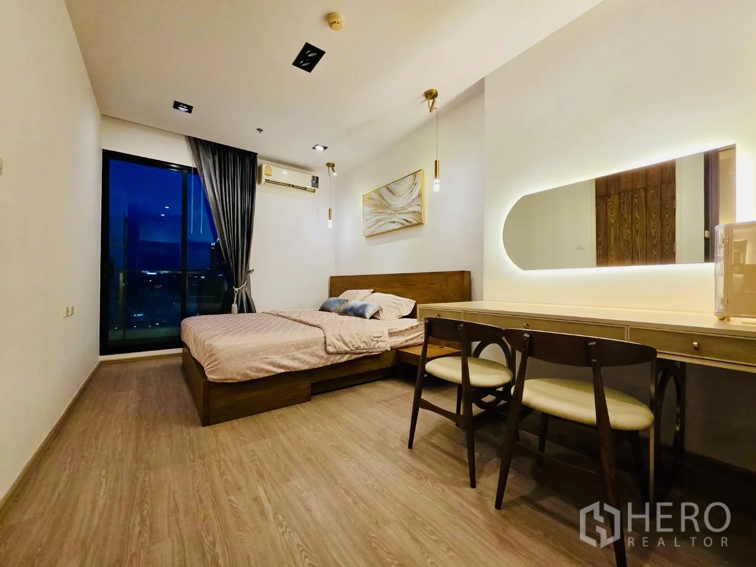 Condominium for rent in Huai Khwang, Bangkok - Spacious bedroom at night with king bed, long dressing desk, and curtain-lined window.