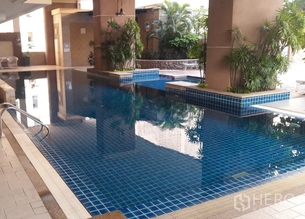 Condominium for rent in Watthana, Bangkok - Condominium facilities with a blue-tiled swimming pool surrounded by greenery and seating.