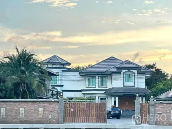 独立式住宅 出售在Khlong Luang, Pathum Thani - 两层独栋别墅，灰色瓦顶，砖墙与木门围合，傍晚景色（空銮县）。