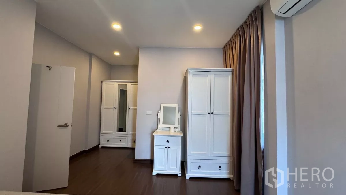 บ้าน ให้เช่าหรือขายในSaphan Sung, Bangkok - มุมห้องนอนพร้อมตู้เสื้อผ้าสีขาวชุดเข้ากันและโต๊ะเครื่องแป้งขนาดกะทัดรัดข้างหน้าต่างติดผ้าม่าน.