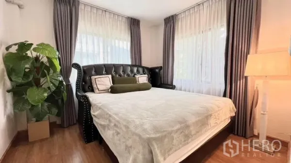 บ้าน ให้เช่าหรือขายในBang Khen, Bangkok - ห้องนอนพร้อมหัวเตียงหนังทรงวินเทจ โคมไฟหัวเตียง และต้นไม้ตกแต่ง