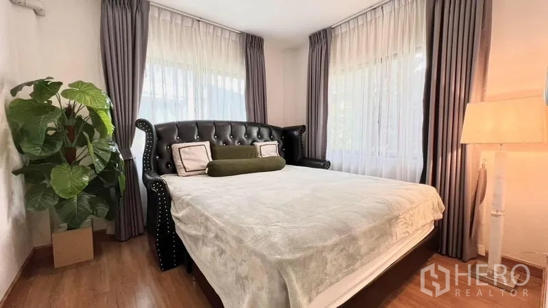 บ้าน ให้เช่าหรือขายในBang Khen, Bangkok - ห้องนอนพร้อมหัวเตียงหนังทรงวินเทจ โคมไฟหัวเตียง และต้นไม้ตกแต่ง