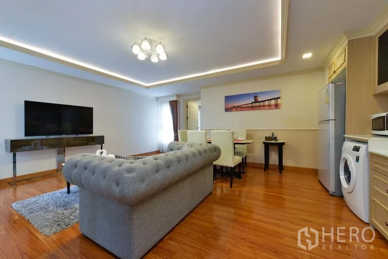 Apartment for rent in Khlong Toei, Bangkok - Living area featuring tufted sofa, coffee table, TV console and wood floors beside dining zone.