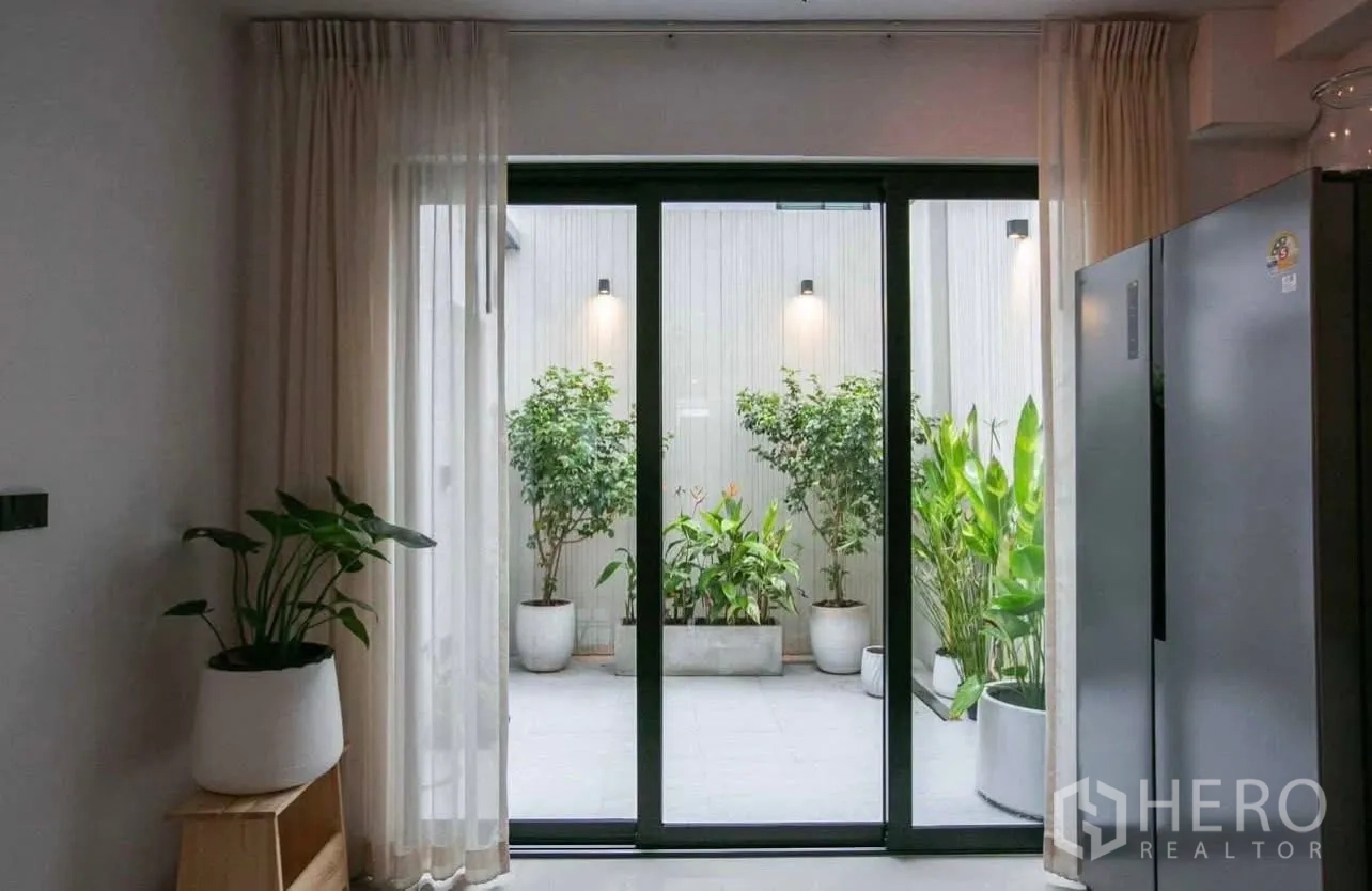 Townhouse for rent in Suan Luang, Bangkok - Sliding glass doors open to a small courtyard garden with potted plants.