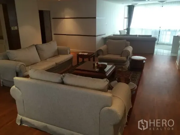 公寓 出租在Khlong Toei, Bangkok - 开放式起居区，数组米色沙发与扶手椅，大窗采光充足，木地板。