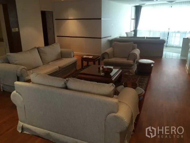 公寓 出租在Khlong Toei, Bangkok - 开放式起居区，数组米色沙发与扶手椅，大窗采光充足，木地板。