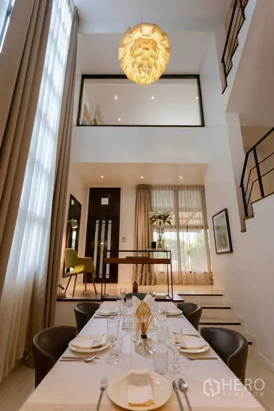 Home Office for sale in Watthana, Bangkok - Double-height dining area with chandelier, mezzanine and staircase in a modern home office.