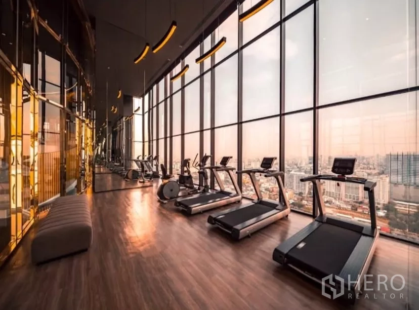 Condominium for rent in Chatuchak, Bangkok - Sky fitness center with treadmills and floor-to-ceiling windows at sunset.