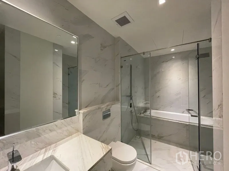 Condominium for rent or sale in Bangkok - Modern marble bathroom featuring a glass-enclosed shower and separate bathtub.