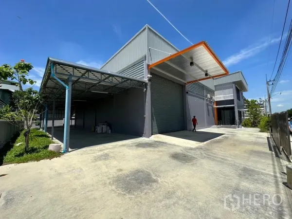 工厂 出租或出售在Lam Luk Ka, Pathum Thani - 工厂外观另一视角，卷闸门、雨棚与宽阔场地一览。