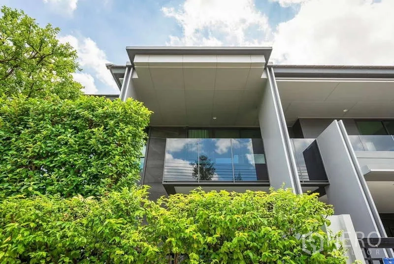 Detached House for rent or sale in Bang Kapi, Bangkok - Upper exterior with glass balcony framed by lush green hedges.