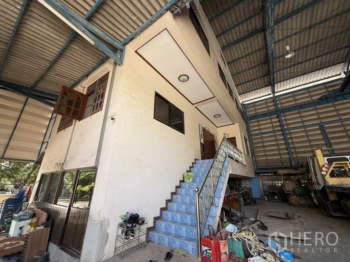 Warehouse for sale in Phra Samut Chedi, Samut Prakan - Two‑storey office/house inside high‑bay warehouse with blue tiled staircase and steel roof.