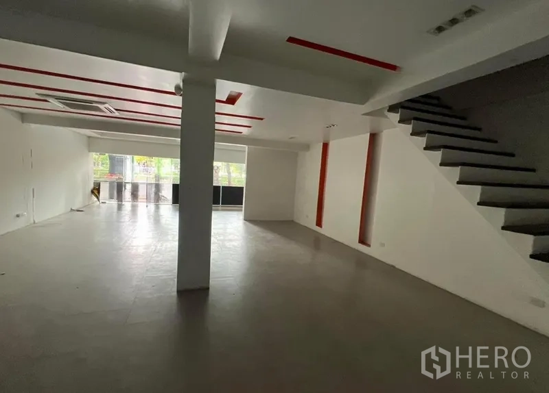 店屋 出租在Watthana, Bangkok - 店屋一层开放式空间，红色吊顶、瓷砖地面、整面落地窗与侧边楼梯。