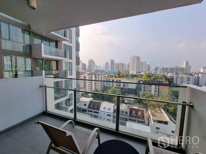 Condominium for rent in Watthana, Bangkok - Covered balcony with glass railing, outdoor chairs and wide skyline view.