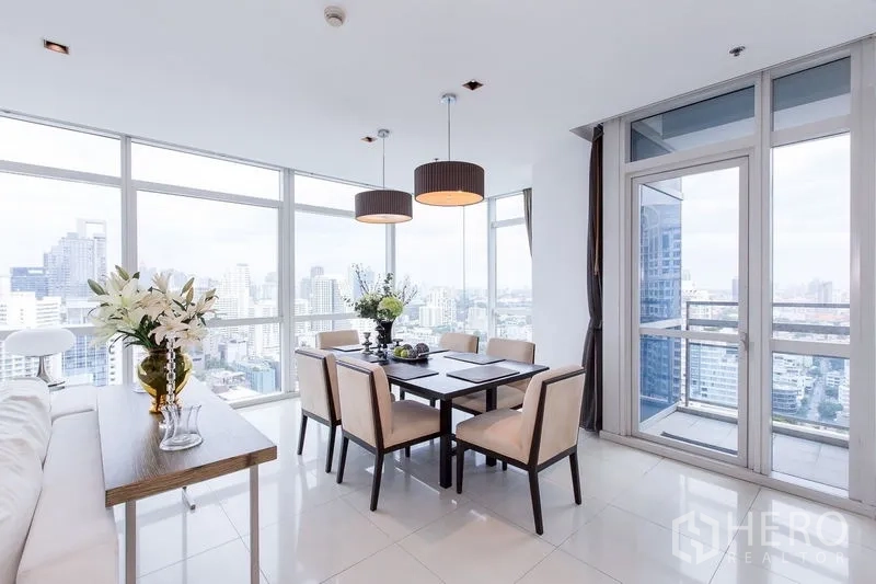 Condominium for rent in Pathum Wan, Bangkok - Corner dining area by panoramic windows with twin pendant lights and a door to a small balcony.
