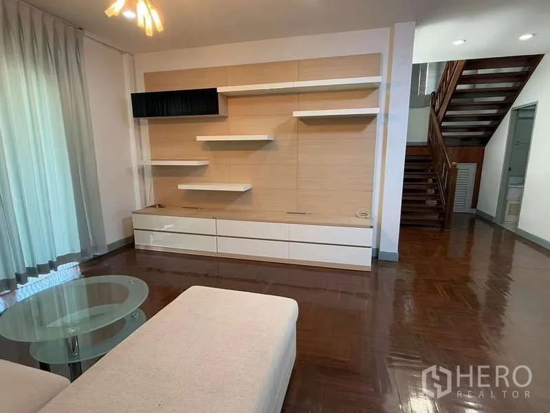 Detached House for rent in Bang Kapi, Bangkok - Bright living room with built‑in media wall, floating shelves and a wooden staircase.