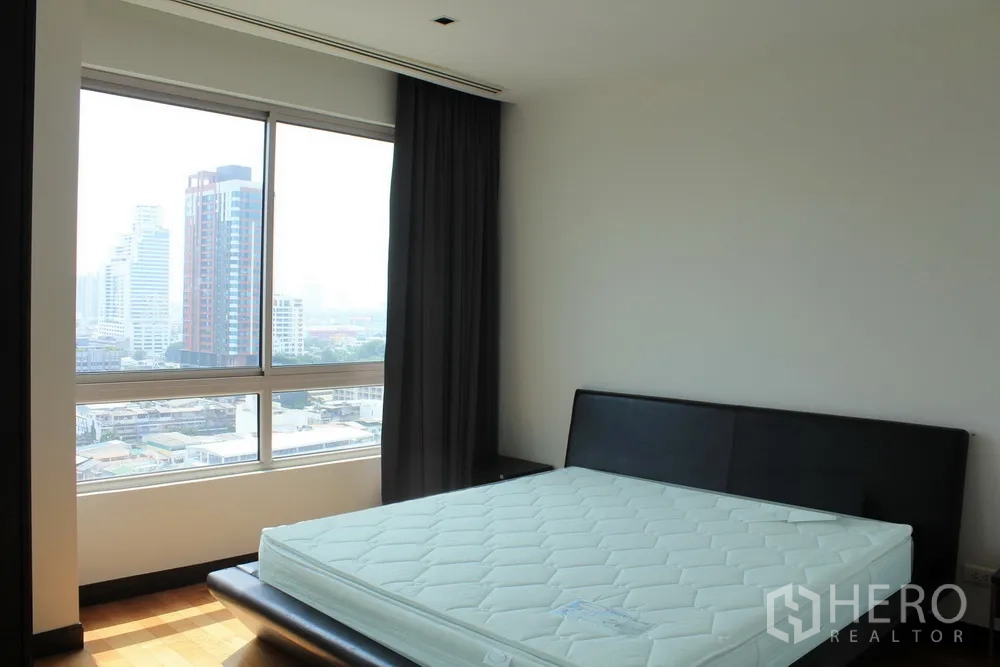 Condominium for rent or sale in Yan Nawa, Bangkok - Bedroom with large window, city views, dark curtains and a mattress on a low black bed frame.