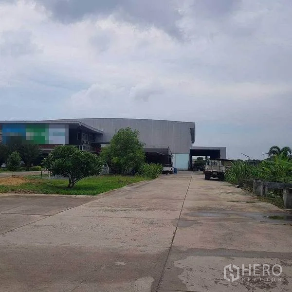 Home Office for sale in Khlong Luang, Pathum Thani - Long driveway leading to the warehouse complex with landscaped greenery along the sides.