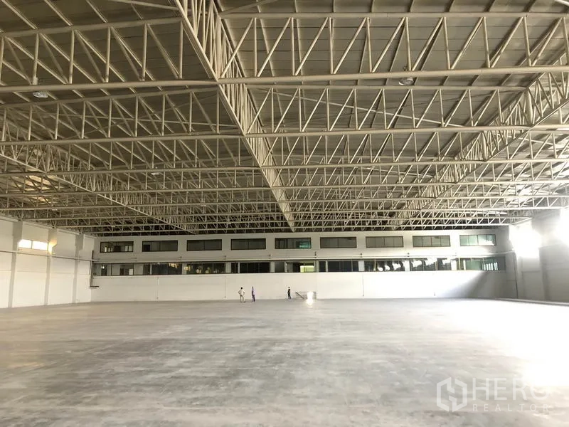 Warehouse for rent in Bang Sao Thong, Samut Prakan - Vast clear-span floor with mezzanine office windows beneath a truss ceiling.